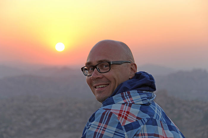 Handsome bald man wearing glasses on a sunset or dawn background in Hampi, India. Beautiful sunset or sunrise. Vijayanagar, karnataka, unesco.